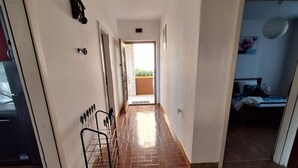 Ένας διάδρομος με πλακάκια στο δ άπεδο, που οδηγεί σε ένα δωμάτιο με ένα κρεβάτι και ένα παράθυρο.