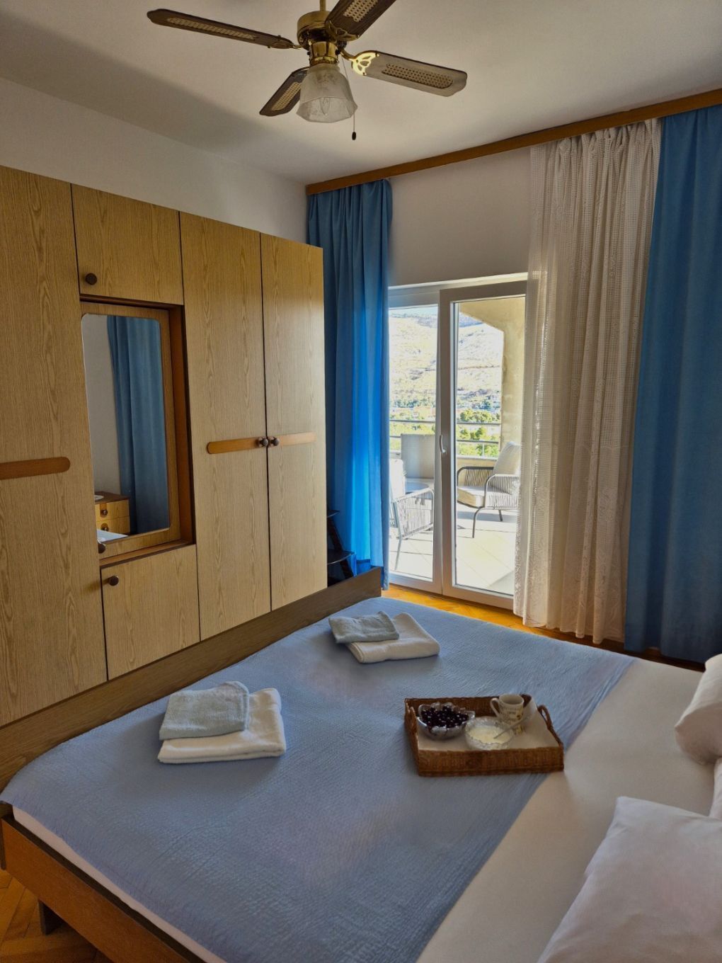 Une chambre à coucher comprenant un lit, une armoire en bois, un ventilateur de plafond et une vue sur l’extérieur grâce à une porte vitrée.
