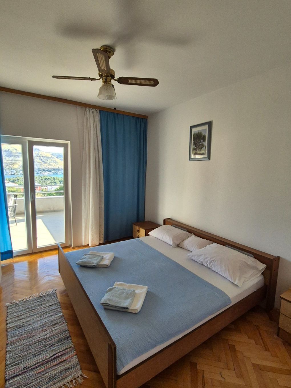 A bedroom with a bed, a ceiling fan, a window with curtains, and a view of the outdoors.