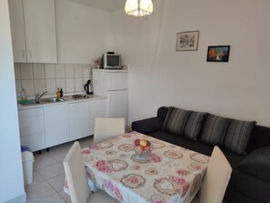 A compact living space with a kitchenette, a dining area with a table and chairs, and a sofa with cushions. - Apartments Josi (Sibenik)