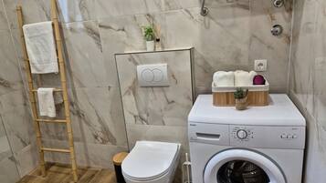 A bathroom with a marble wall, a washing machine, a toilet, and a towel rack.