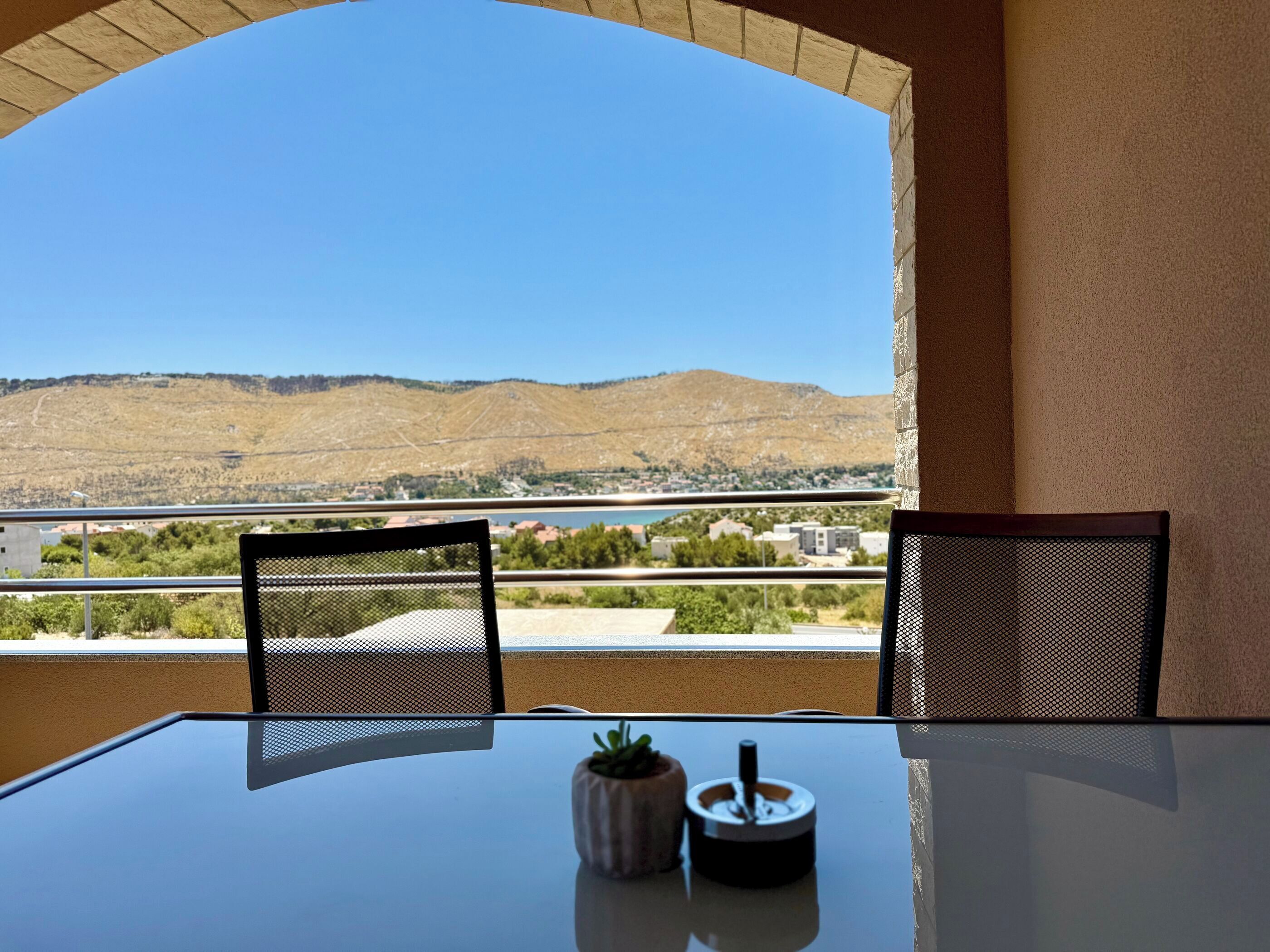 A balcony with a table, chairs, and a view of a hilly landscape.