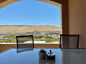 A balcony with a table, chairs, and a view of a hilly landscape. - Apartments Josi (Sibenik)