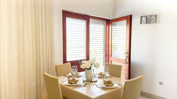 Un comedor con una mesa dispuesta para cuatro, un florero con flores blancas y una ventana con persianas.
