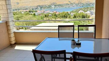 A balcony with a table and chairs, a view of a lake, and a mountainous landscape.