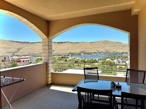 A balcony with a table and chairs, a clothes drying rack, and a view of a lake and hills. - Apartments Josi (Sibenik)
