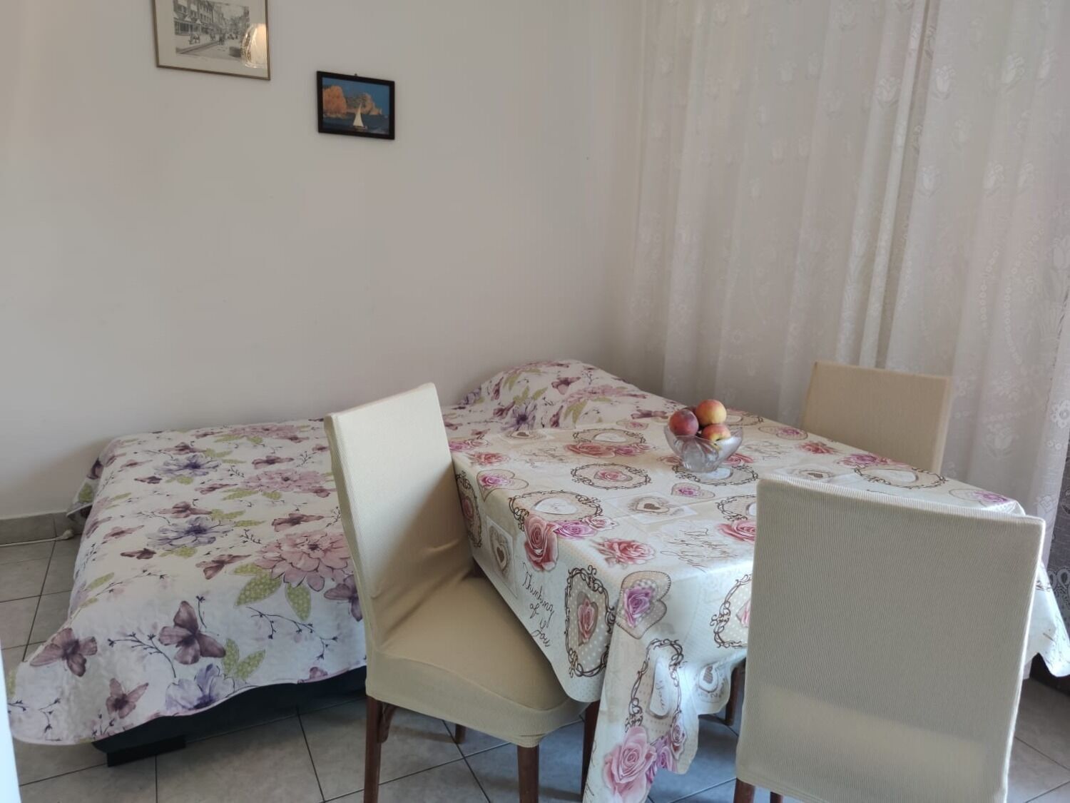 Un comedor con una mesa dispuesta para dos personas, cubierta con un mantel estampado de flores, y dos sillas.