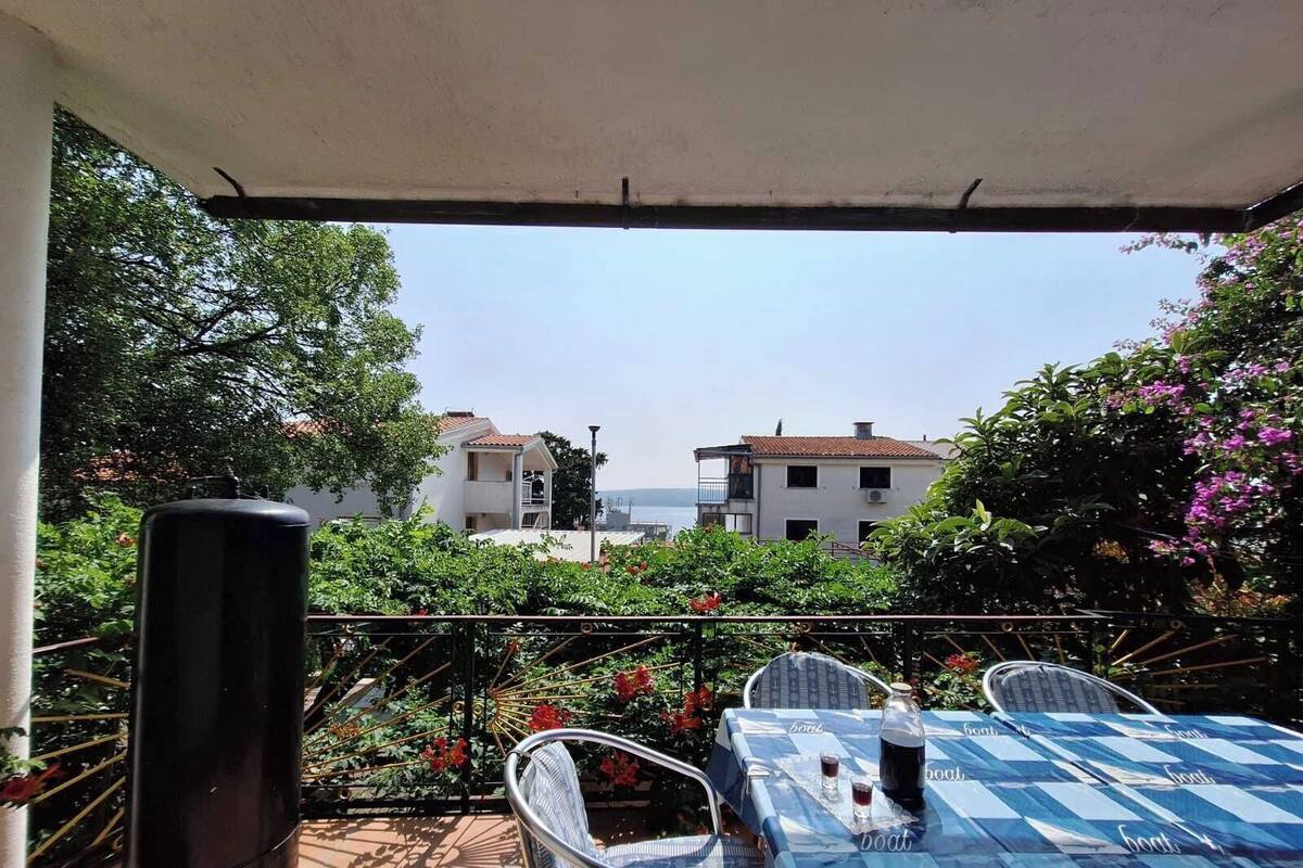 An outdoor patio with a table set for two, a grill, and a view of buildings and trees.