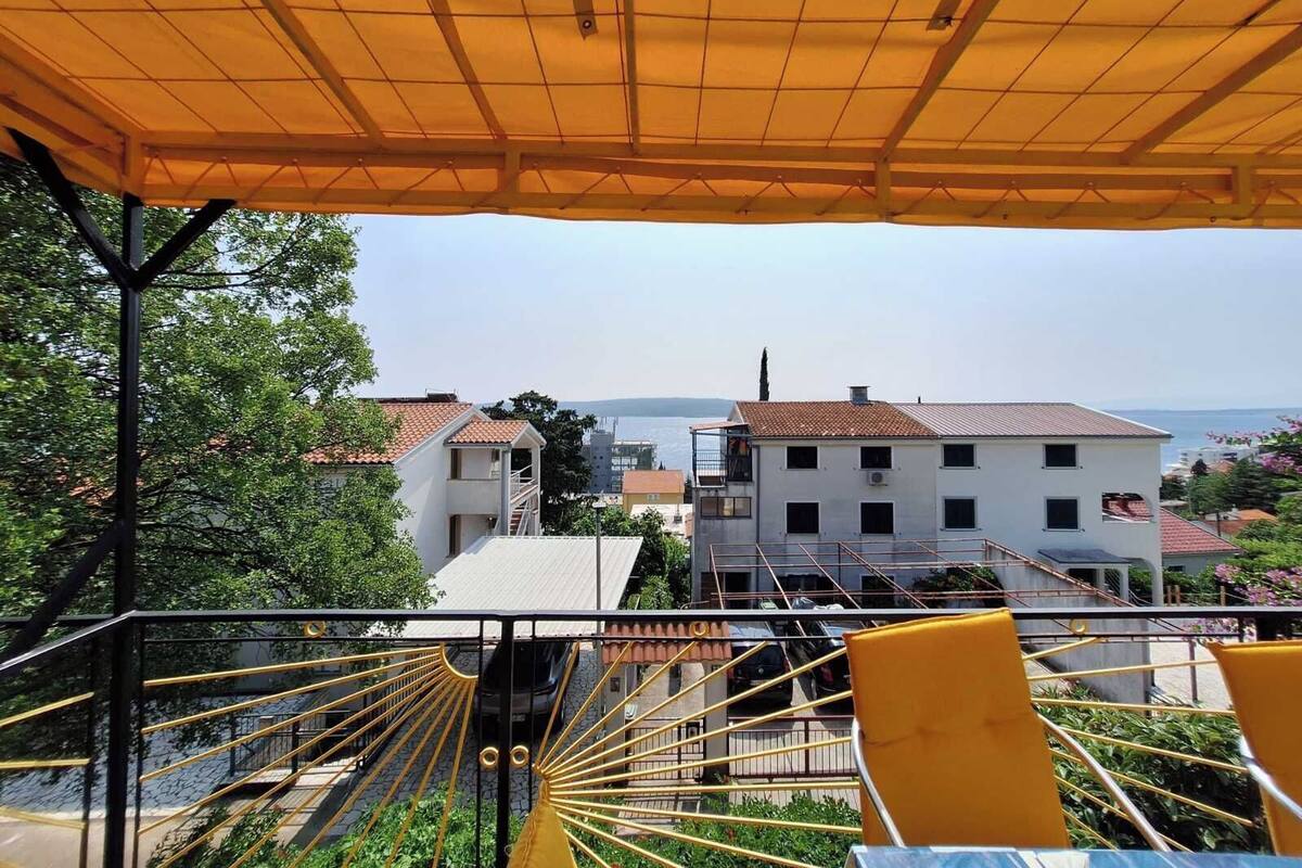 A terrace with yellow chairs and a table, overlooking a coastal area with buildings and a view of the sea.