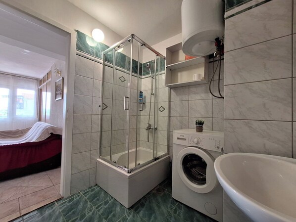 A bathroom with a glass-enclosed shower, a washing machine, and a sink. - Apartment Ivy (Crikvenica)