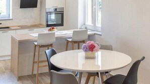 Une cuisine moderne dotée d’un îlot central, d’un coin repas avec une table ronde et des chaises, et d’une grande fenêtre qui laisse entrer la lumière naturelle.