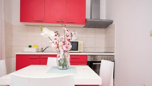 A kitchen with red cabinets, a white table, and a vase with flowers. - Apartments Ljubo (Vrsi)