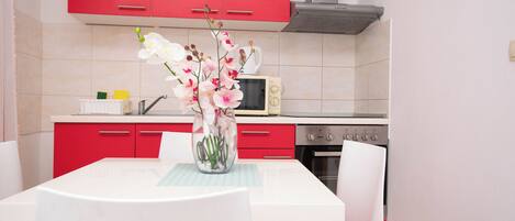 A kitchen with red cabinets, a white table, and a vase with flowers.
