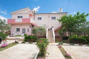 A two-story building with a balcony, a staircase, and a garden with various plants and flowers. - Apartments Ljubo (Vrsi)