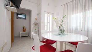 A dining area with a round table, white chairs, and a vase with flowers. - Apartments Ljubo (Vrsi)