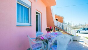 A pink building with a patio area featuring a table and chairs, a staircase, and a parked car. - Apartments Ljubo (Vrsi)