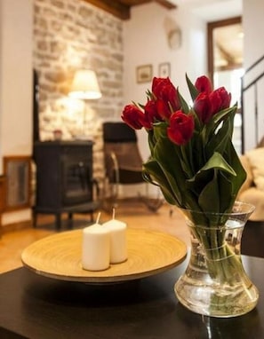 Ein Wohnzimmer mit Steinwand, Kamin, Tisch mit Kerzen und einer Vase mit roten Blumen.