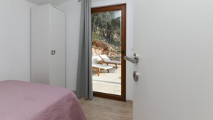 Ein Schlafzimmer mit einem Bett, einer Tür zu einem Außenbereich mit einer Bank und Blick auf Bäume.