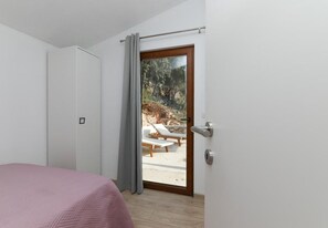 A bedroom with a bed, a door leading to an outdoor area with a bench and a view of trees. - House Irena (Pucisca)