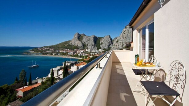 Ein Balkon mit Tisch und Stühlen, mit Blick auf eine Küstenstadt und das Meer.