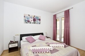 A bedroom with a bed, a nightstand, a painting, and a window with curtains. - House Miho (Omis)