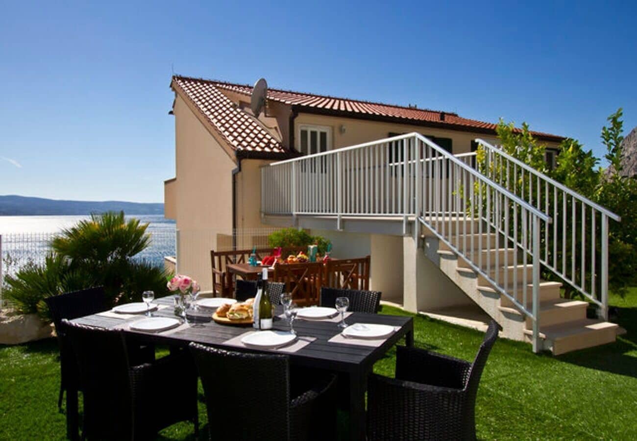 Un coin repas avec une table dressée pour quatre personnes, un escalier et une vue sur la mer.