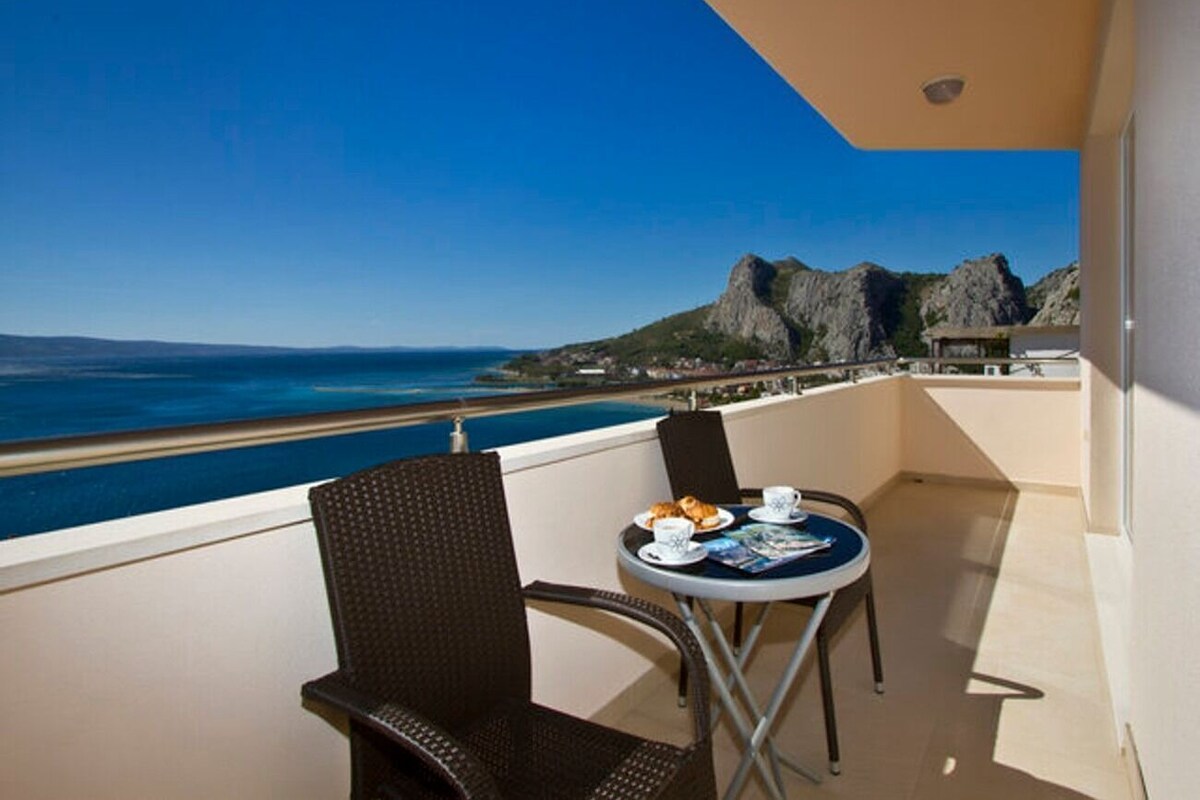 A balcony with a table and chairs, overlooking a beach and rocky cliffs.