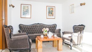 A room with a dark upholstered sofa, two armchairs, a wooden coffee table with a vase of flowers, and framed artwork on the walls. - House Villa Oaza (Rogoznica)