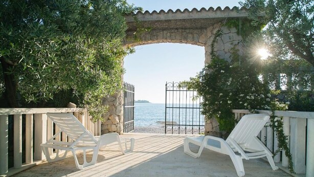A stone archway leading to a beach with white lounge chairs and a gate. - House Villa Oaza (Rogoznica)