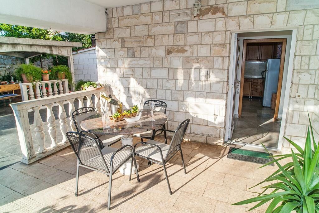 An outdoor patio with a stone wall, a dining table with chairs, and a kitchen visible through an open door.