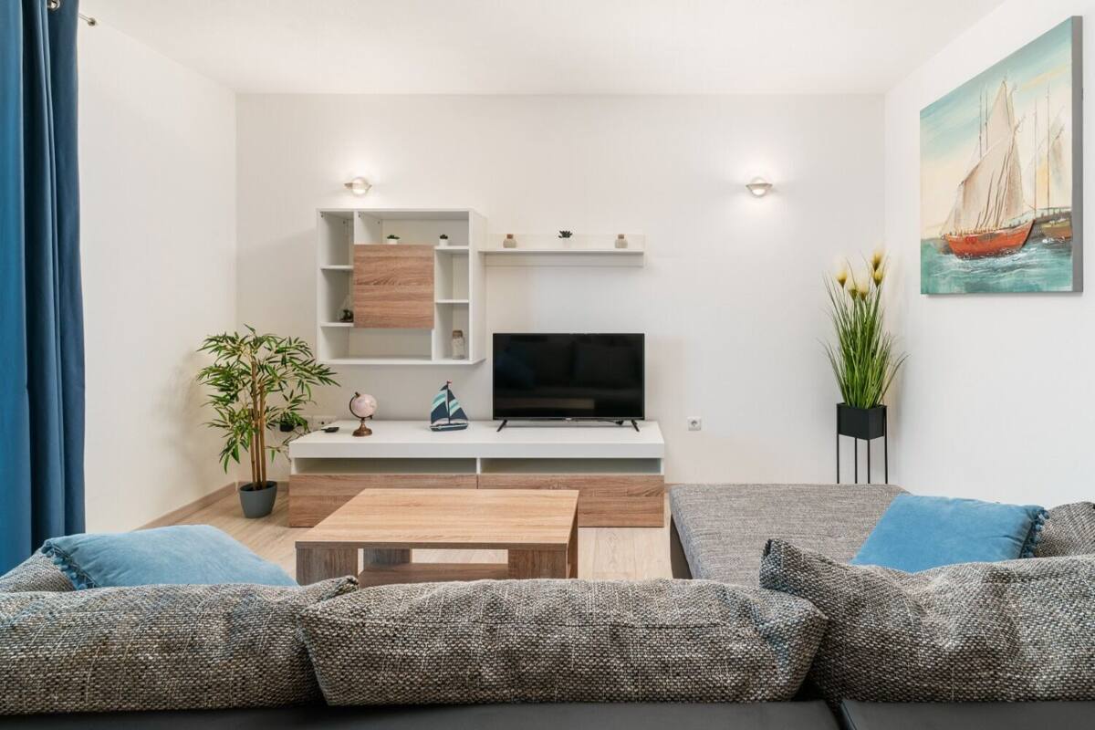 A modern living room with a flat-screen TV, wooden shelves, a coffee table, and a sofa with blue cushions.