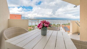 A balcony with a table and chairs, a vase of flowers, and a view of the sea and buildings. - Apartment The View (Trogir)