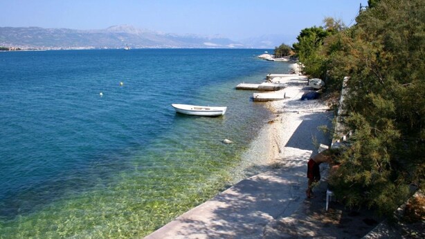 A clear coastal view with a boat on the water, a sandy beach, and a person walking along the shore. - Apartment The View (Trogir)
