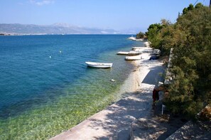 A clear coastal view with a boat on the water, a sandy beach, and a person walking along the shore. - Apartment The View (Trogir)