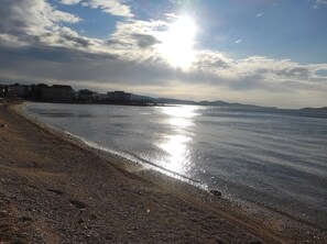 A beach with a clear sky, calm water, and distant buildings. - Apartment Jase Beachfront (Sibenik)