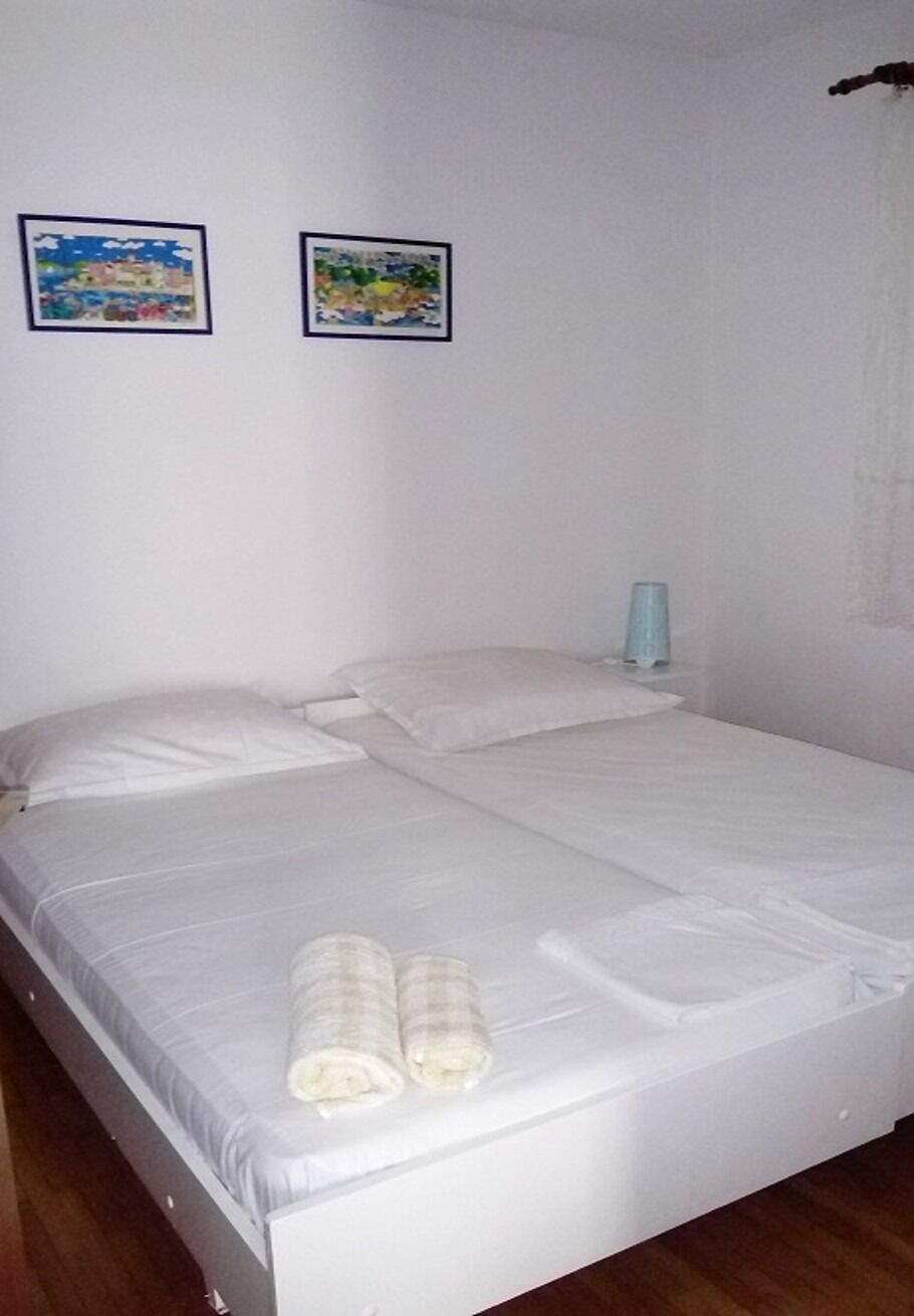 Quarto de casal com cama de casal, roupa de cama branca, duas obras de arte emolduradas na parede e abajur.