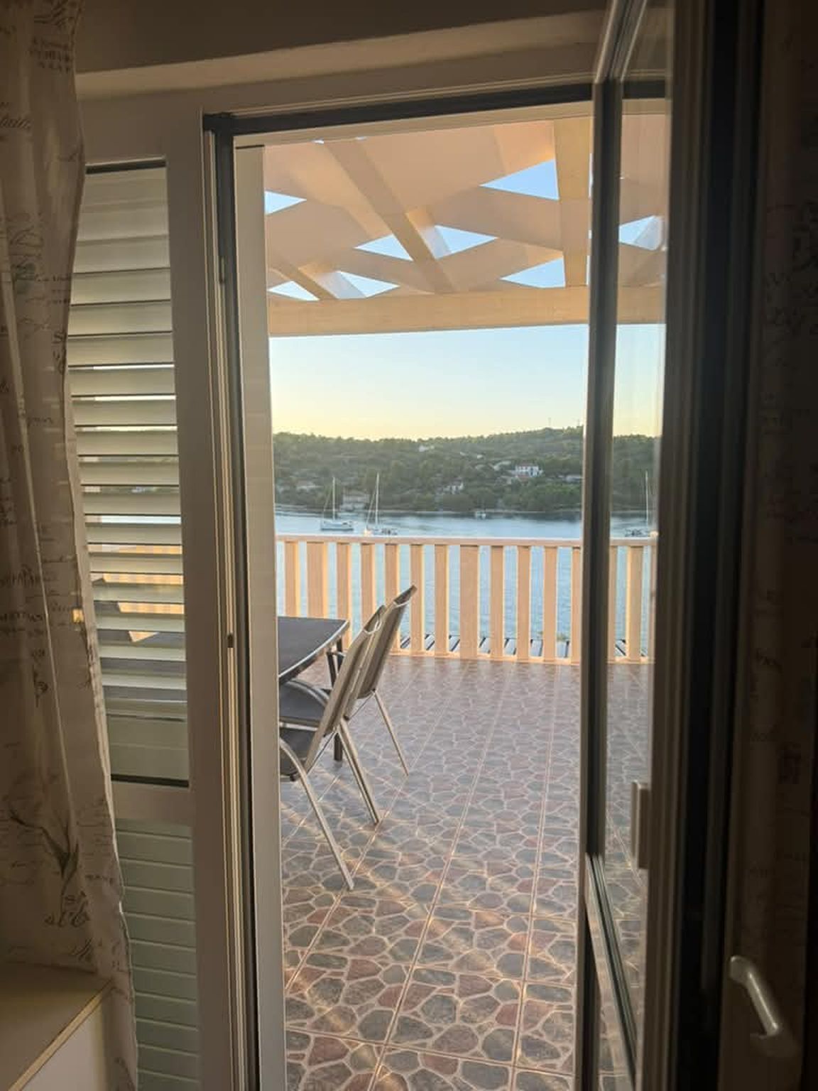 A view from a room with a sliding glass door to an outdoor patio with a tiled floor and a table with chairs.