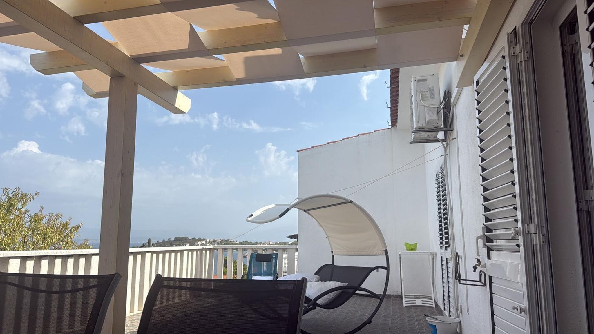 Uma varanda com pérgola, duas cadeiras, uma mesa pequena e vista para o mar.