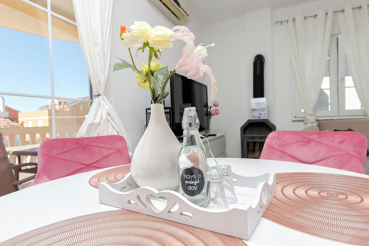 Una mesa de comedor con un jarrón blanco con flores, una botella con etiqueta y una bandeja con forma de corazones.