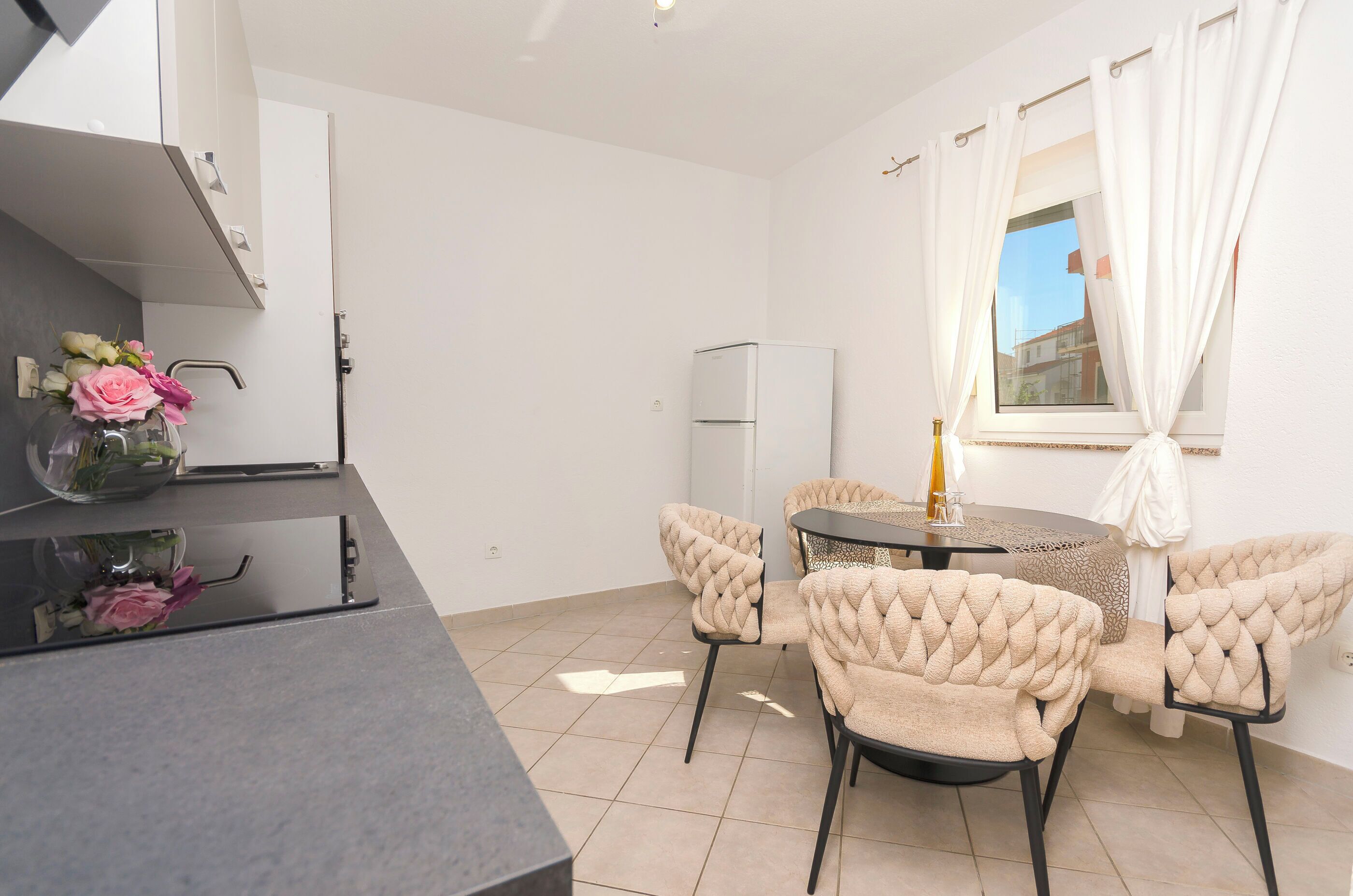 A modern kitchen with white cabinets, a built-in oven, and a dining area with tufted chairs and a round table.