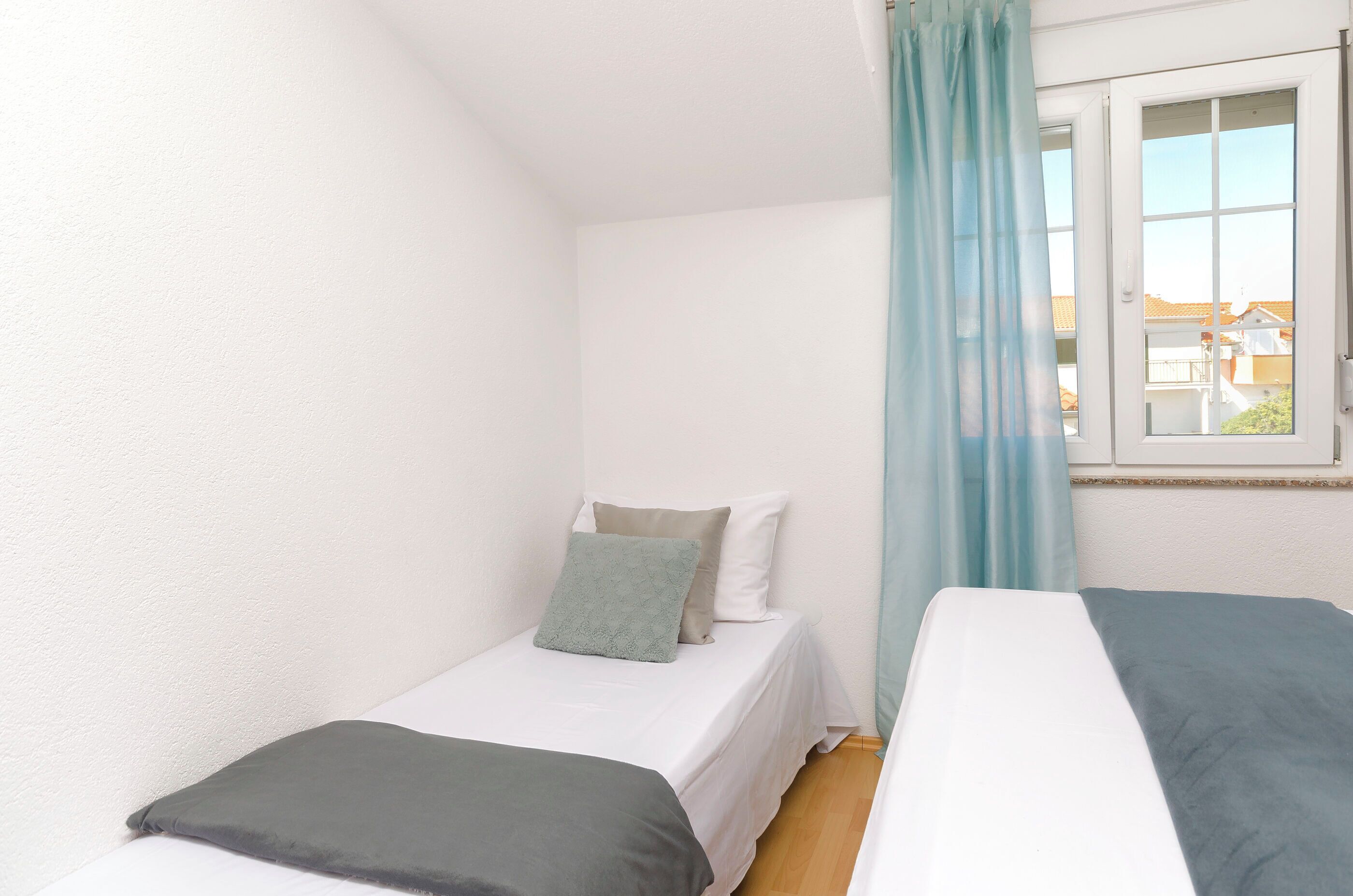 Une petite chambre avec un lit simple, une fenêtre et un rideau.