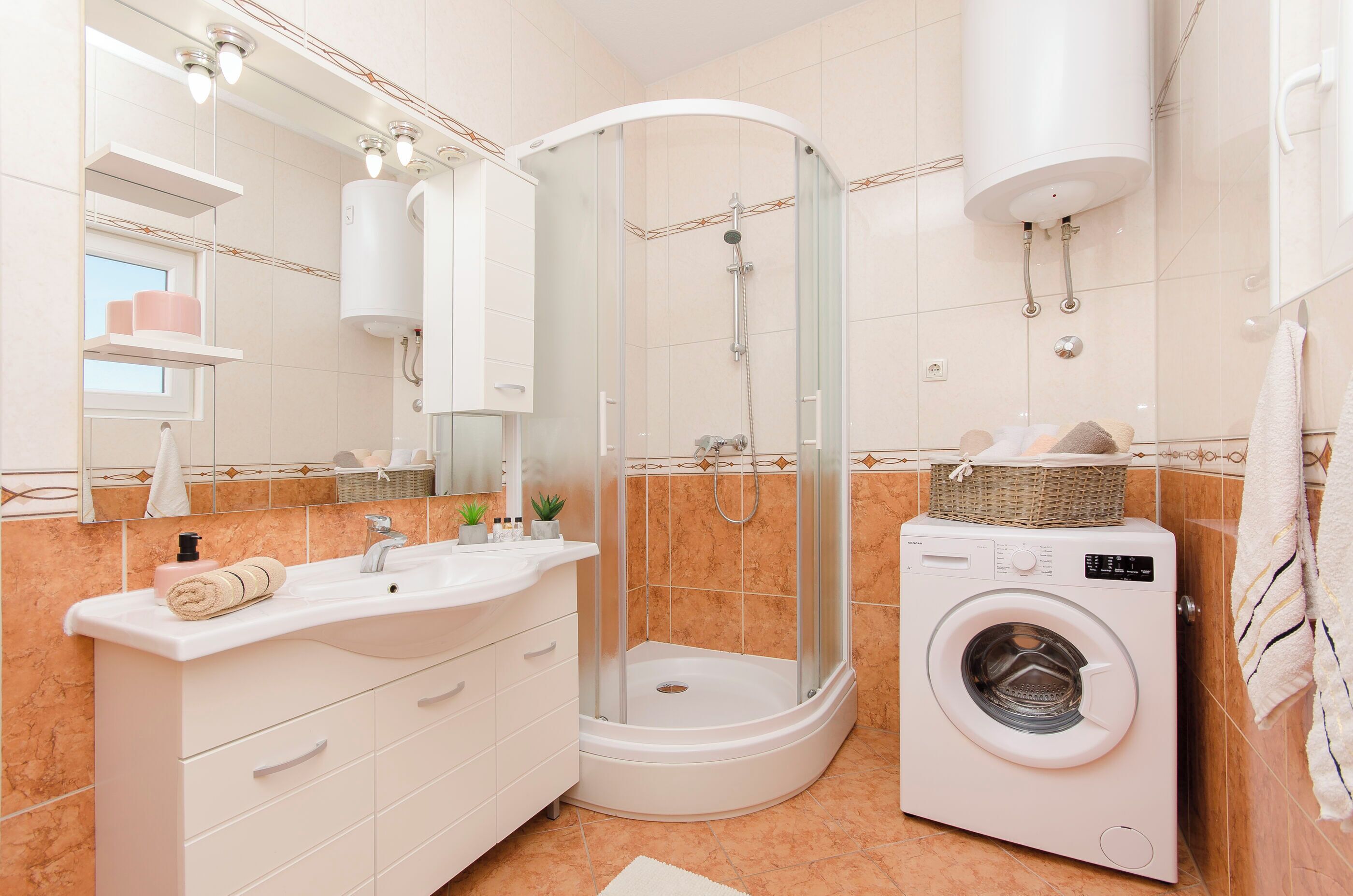 Une salle de bain moderne dotée d’une douche à parois de verre, d’un lave-linge encastré et d’un meuble-lavabo avec un évier et un miroir.