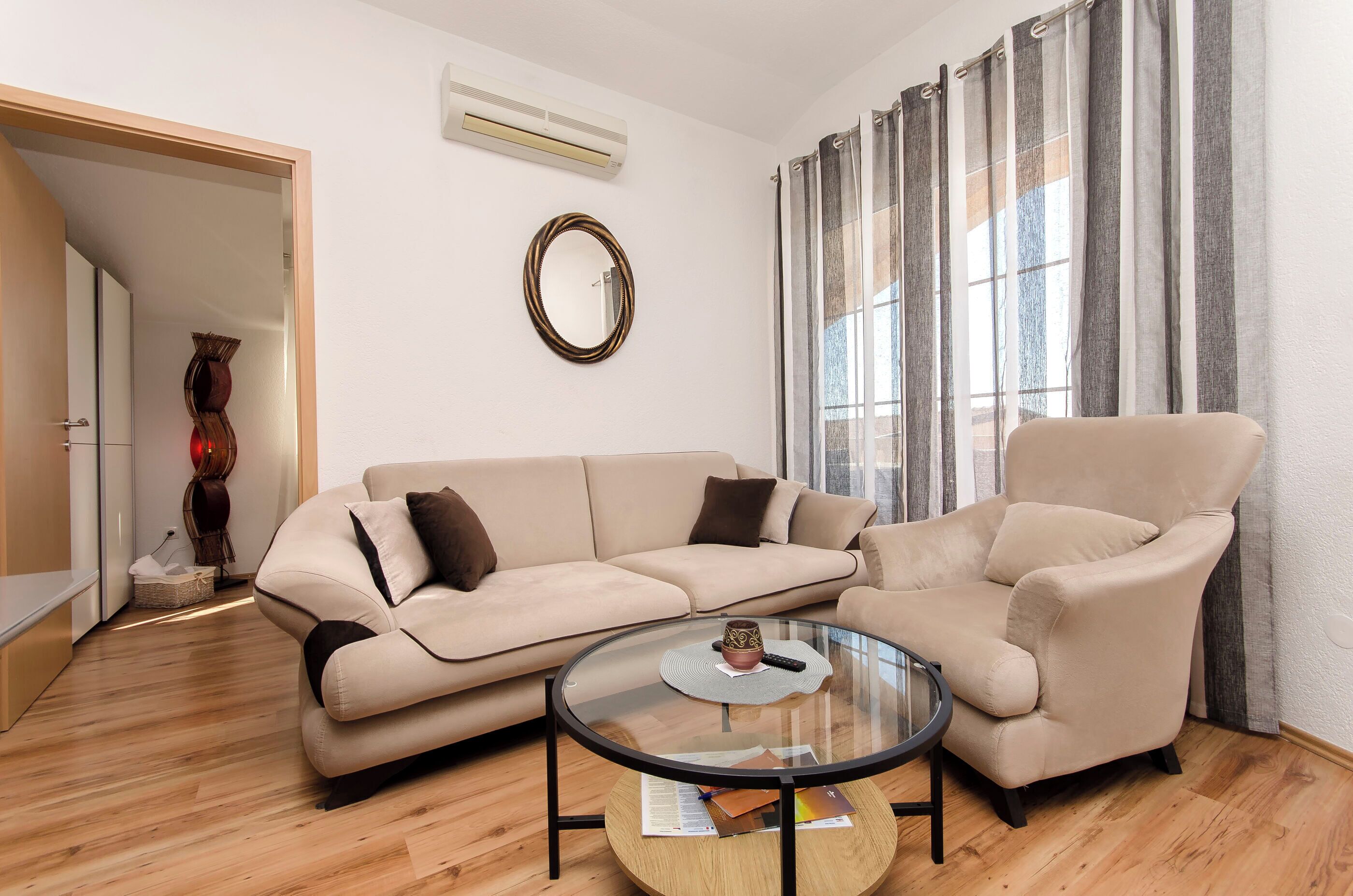 A living room with a beige sectional sofa, a round glass coffee table, and a beige armchair.