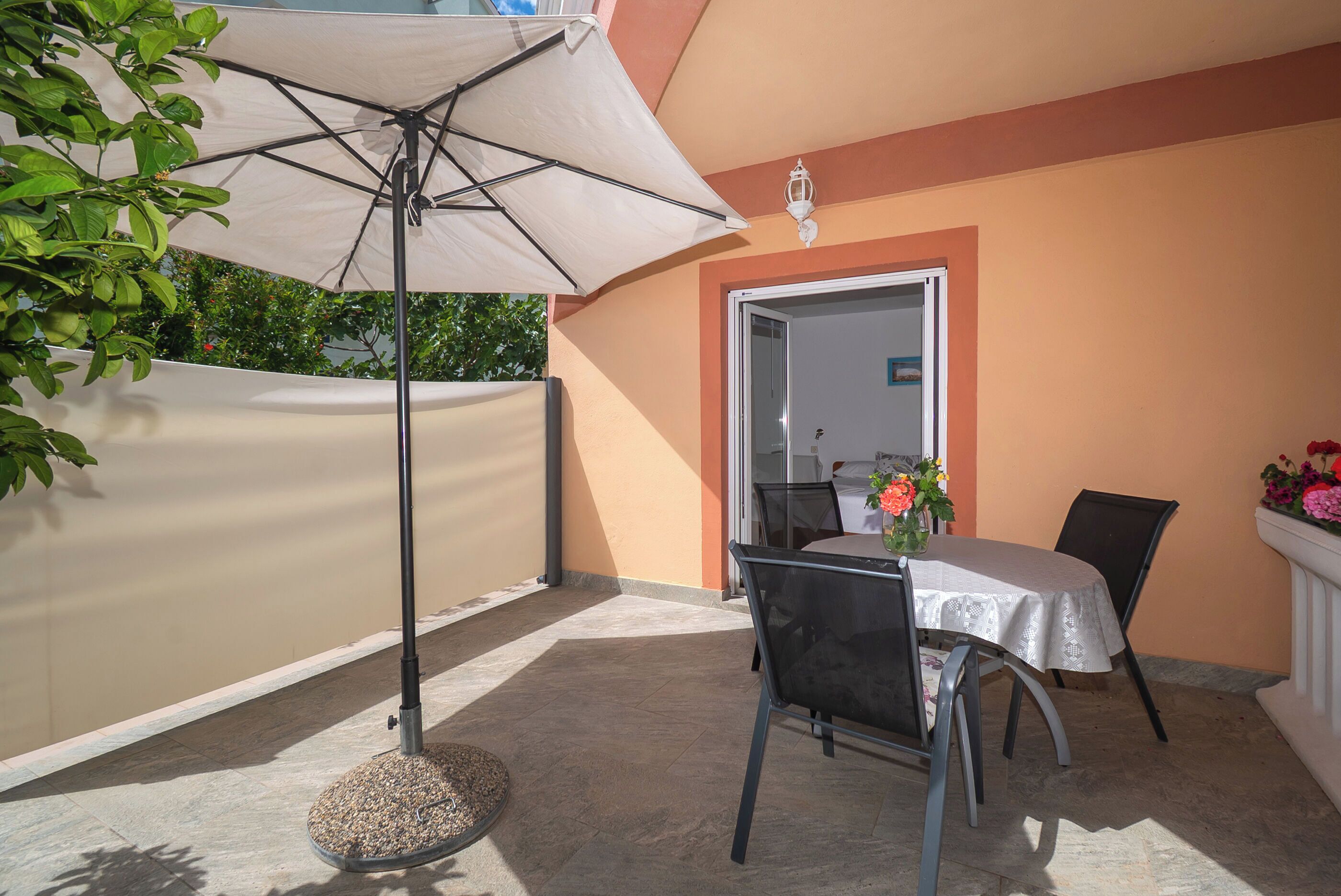 An outdoor patio with a table and chairs, a round table with a white tablecloth, and a large umbrella providing shade.