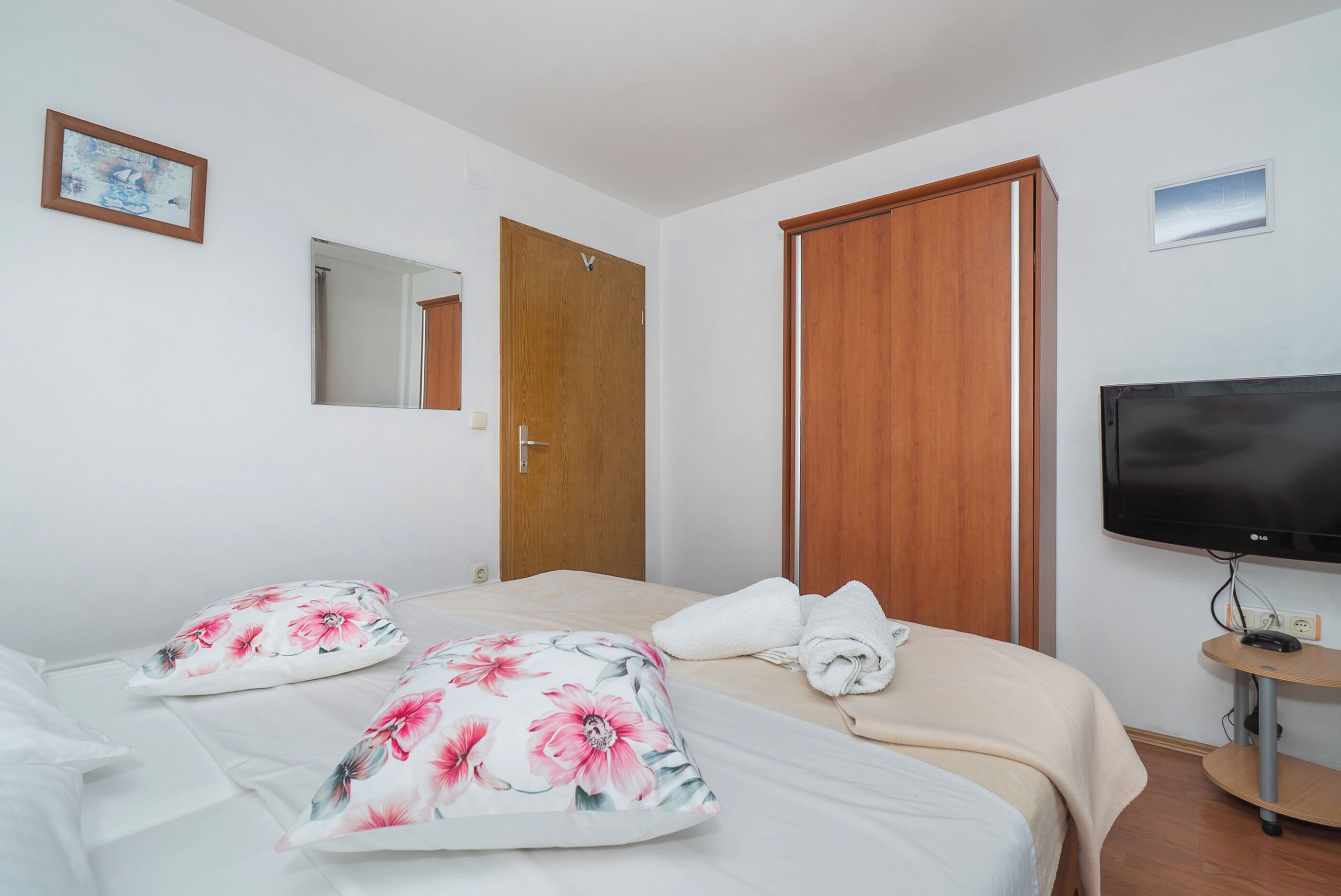Habitación de hotel con cama, dos almohadas, televisor, armario de madera y espejo.