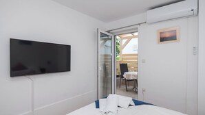 A hotel room with a bed, a TV mounted on the wall, a sliding glass door leading to an outdoor area, and a small table with chairs. - Apartments Jak (Vodice)