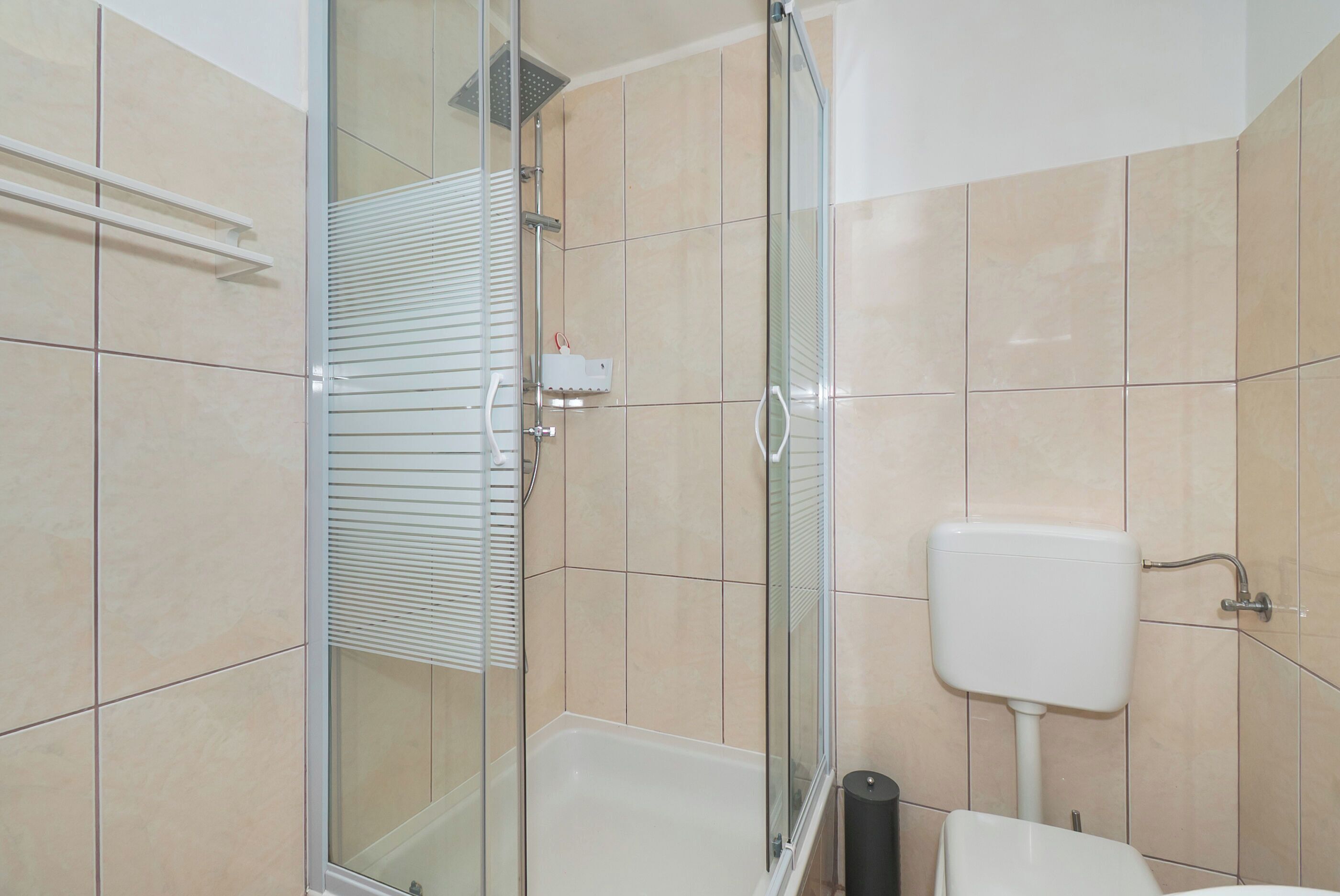 Et moderne badeværelse med et glasafskærmet brusebad, et hvidt toilet og beige vægfliser.