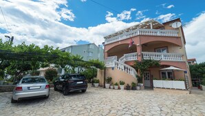 A multi-story building with a balcony, potted plants, and a stone-paved entrance. - Apartments Jak (Vodice)
