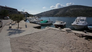Una marina con imbarcazioni ormeggiate, una spiaggia sabbiosa e un paesaggio collinare sullo sfondo.