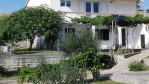 Una casa de dos pisos con un balcón, un jardín con diversas plantas y un cielo despejado.
